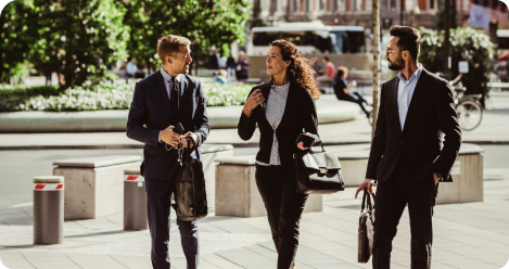 Three business professionals, two men and one woman, walking on a busy city street in daylight.