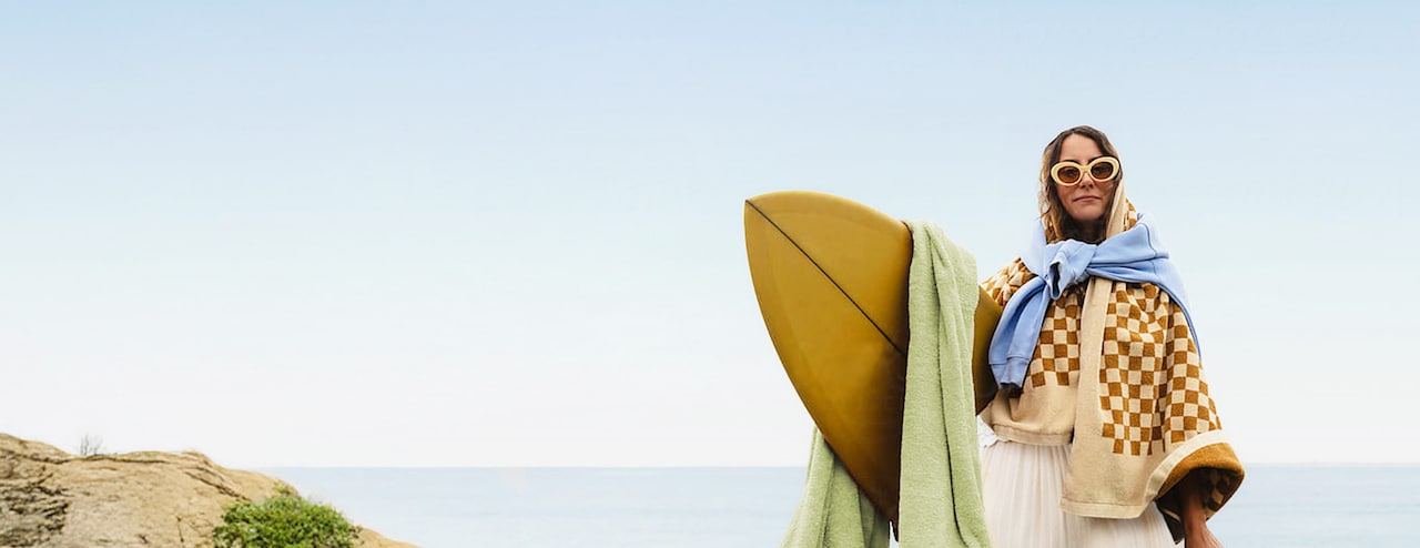 Stylish person on an ocean cliff holding a surfboard on a sunny day.