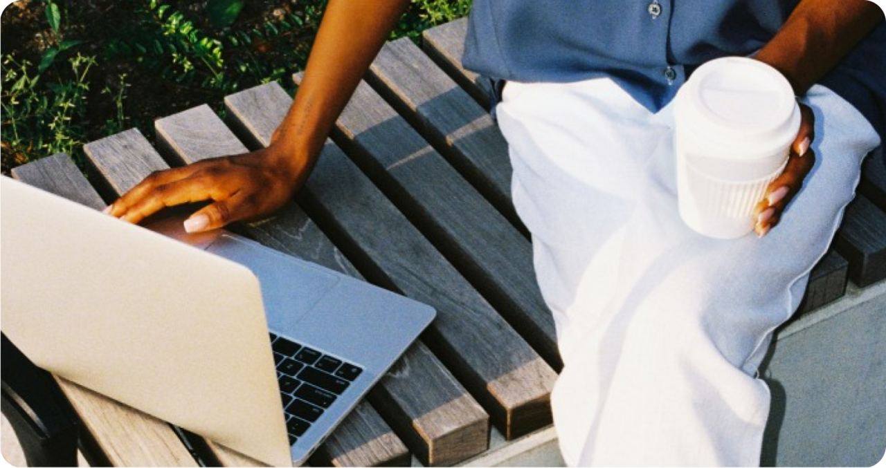 Person working on laptop with a coffee in hand outside on a bench