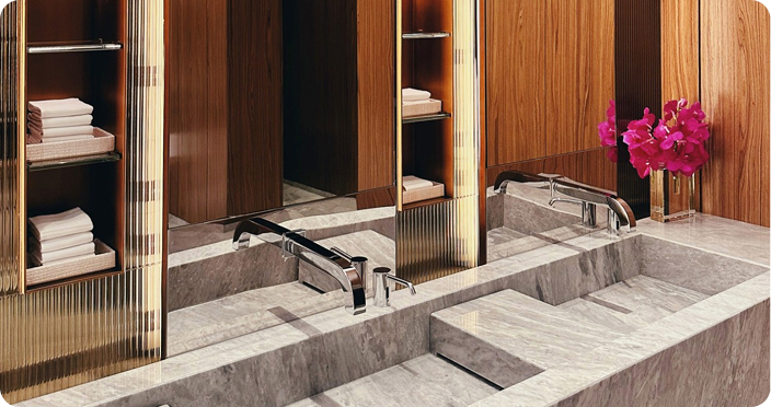 Modern bathroom with marble sink and wooden open shelving with folded towels.