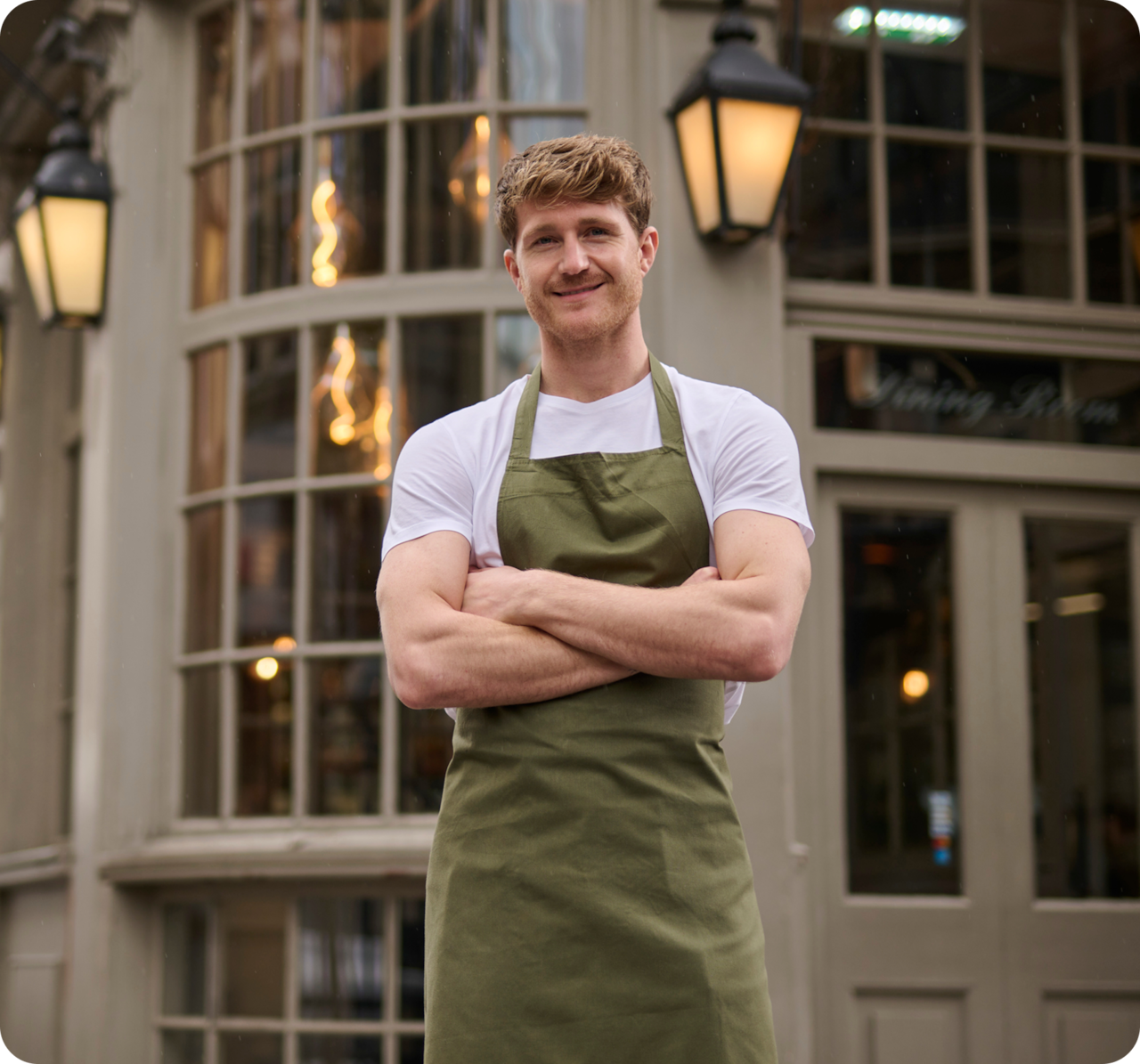 Man wearing a green apron with arms crossed