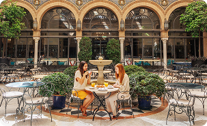 Group of friends enjoying drinks at a European-style courtyard café with arches.