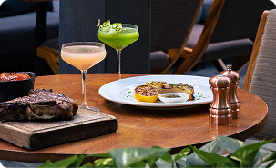 Elegant restaurant table with grilled steak, seared seafood dish, orange cocktail, and green cocktail.
