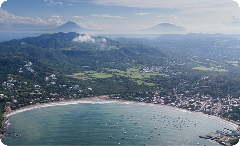Coastal city with a large white domed building near the ocean and mountains in the background.