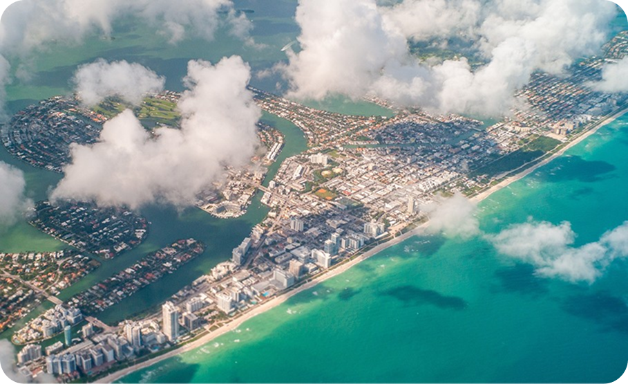 Aerial view of Miami Beach, showcasing a long sandy shoreline with high-rise hotels and turquoise water.