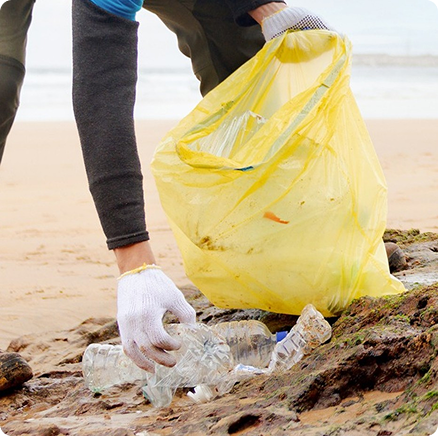 Volunteer with gloved hands picking up littered plastic bottles from a sandy beach.