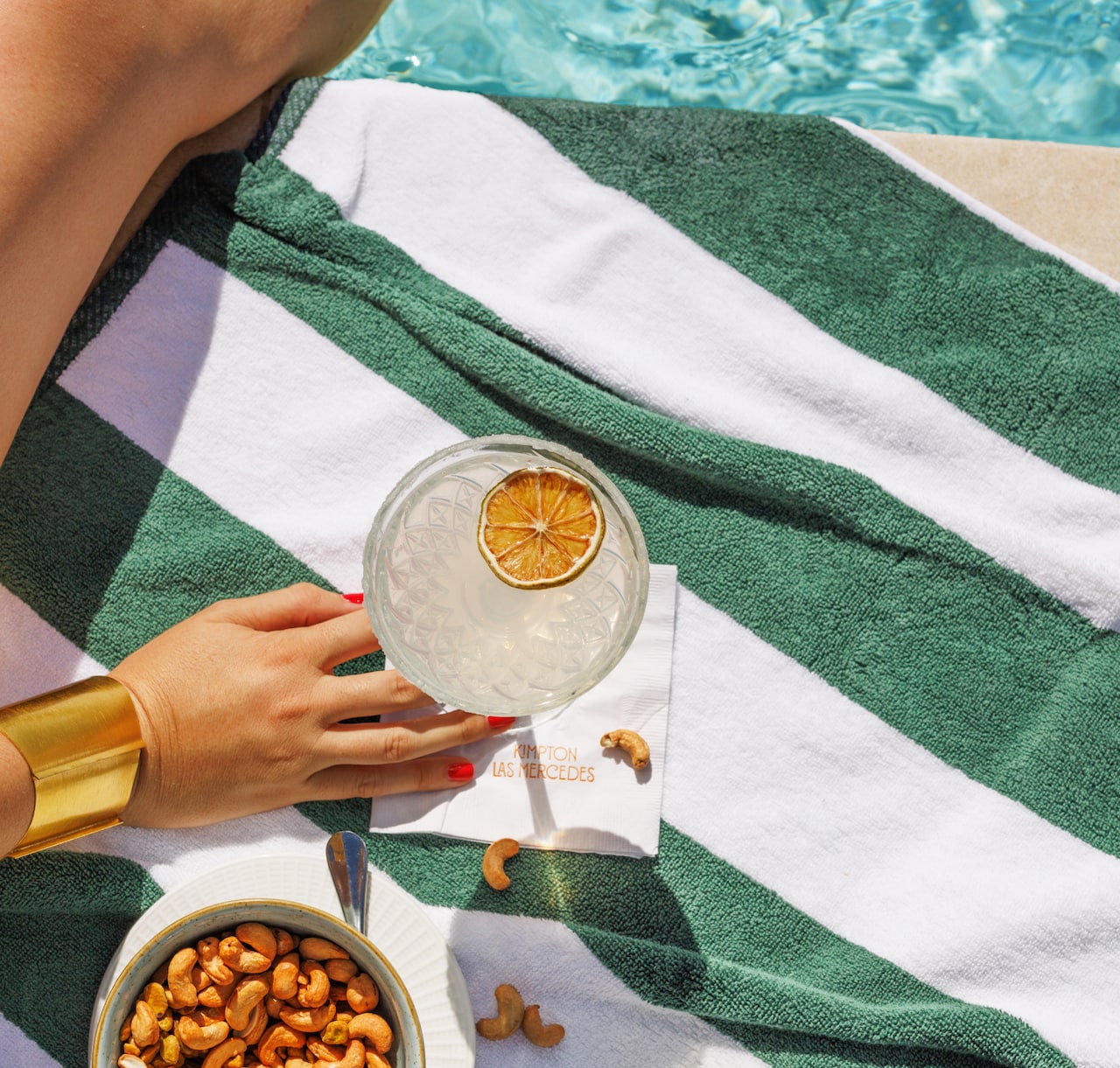 Person relaxing by a pool enjoying a drink on a striped towel